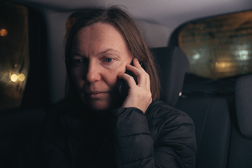 Worried woman talking on mobile phone from the car back seat at night, selective focus