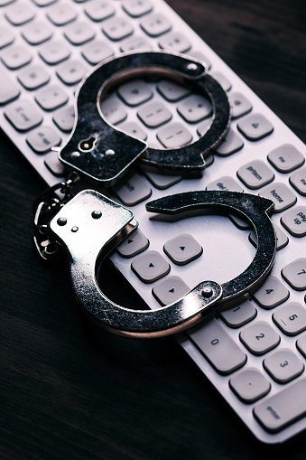 High tech IT cyber crime arrest concept, image of police handcuffs over computer keyboard, selective focus