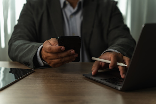 businessman working uses a mobile texting cell phone to contact us business and connect on a desk computer work job at workplaces