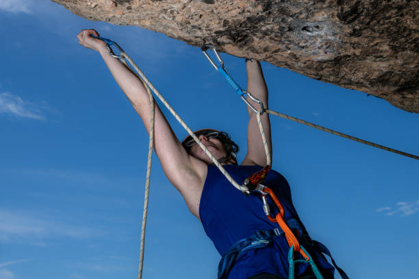A young woman climbs an outdoor rock wall with focused determination, showcasing her active lifestyle and tenacity. Her hands grip firmly, highlighting the strength and effort involved in rock climbing.