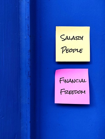 Yellow and Pink note stick on bright blue wall with text written SALARY PEOPLE - FINANCIAL FREEDOM ,concept of setting financial goal from being paid worker to achieve financial freedom