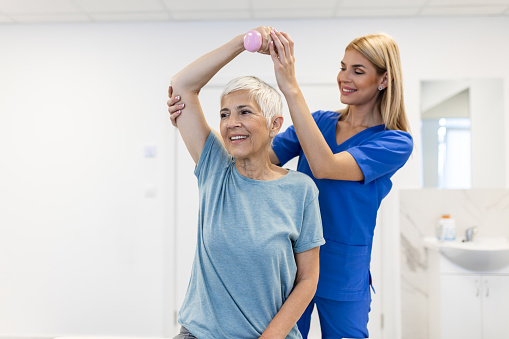 Physiotherapist woman giving exercise with dumbbell treatment About Arm and Shoulder of senior female patient Physical therapy concept