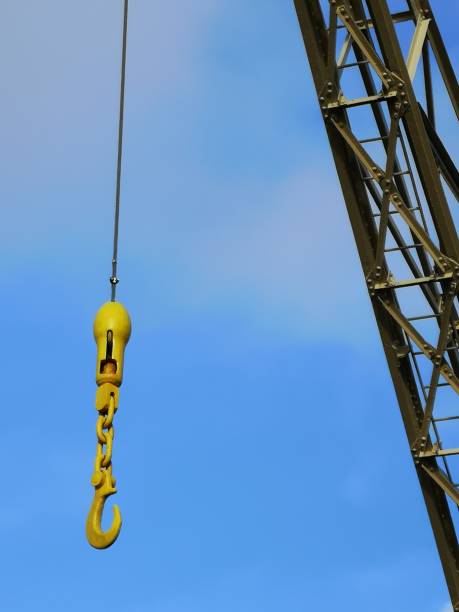 Hanging iron hook from a hoist crane, against a blue sky.