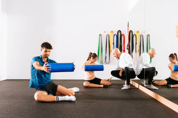 istock Trainer helping woman doing stretching exercise with foam roller at gym class 1916719832