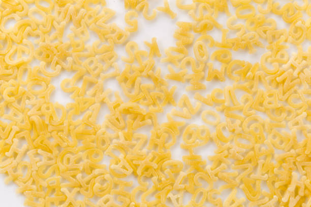 Whole grain dark pasta letters on dark yellow textured background front view with selected focus