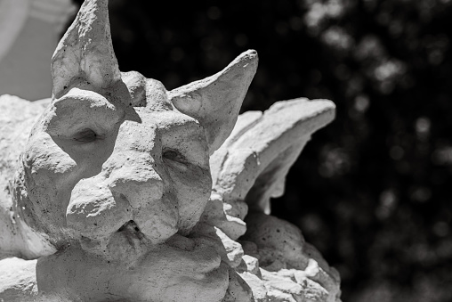 A closeup of a stone gargoyle sculpture on a wall in grayscale