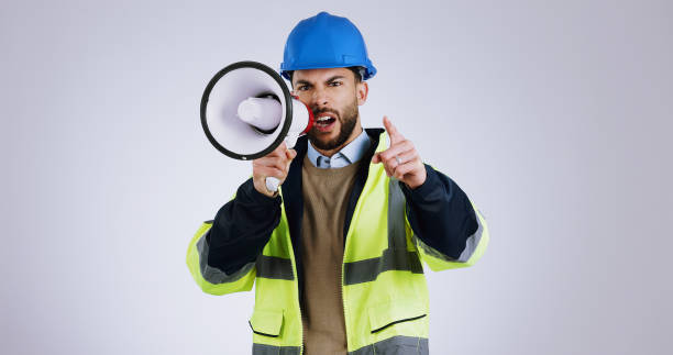 istock Angry man, architect and pointing with megaphone for construction or protest against a gray studio background. Portrait of male person, contractor or engineer shouting or screaming on loudspeaker 1916732520