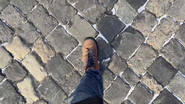 Top view of man's leather boots walking on cobblestone