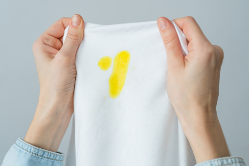 Unrecognizable woman holding white clothes with a yellow stain