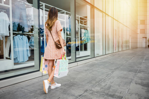 young women walk down a busy street, each carrying shopping bags from their favorite stores - foto stock