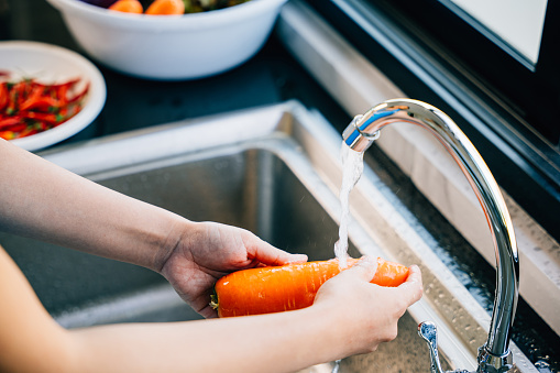 Hygienic vegetable washing, Young woman carefully washes carrots in the kitchen sink for organic cooking. Emphasizing the importance of cleaning vegetables.