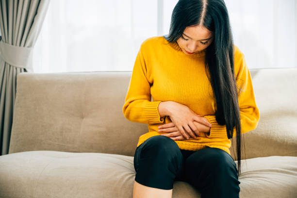 istock Asian woman seated on a home couch experiences abdominal pain 1916760138