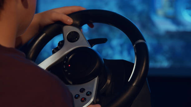 istock Child's hand holding gaming steering wheel against the screen 1916782121