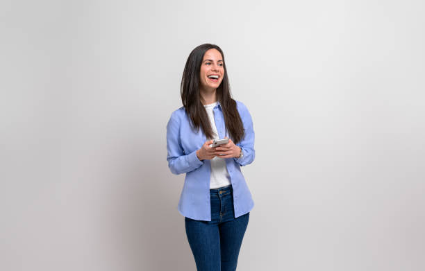 istock Female entrepreneur with mobile phone smiling and looking away while standing on white background 1916785780