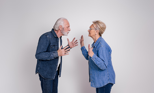 Side view of furious senior husband and wife blaming and fighting while standing on white background