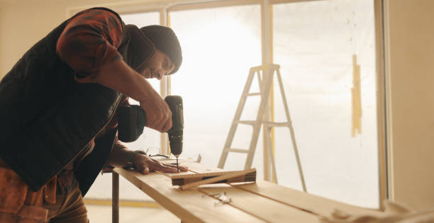 istock Man working with a drill gun to secure a wood plank for trim work 1916790005