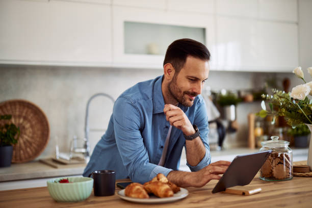 istock A focused adult man checking an email on a tablet while leaning on a kitchen counter. 1916793221