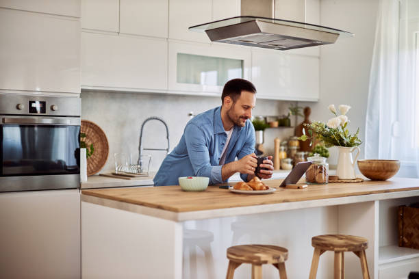 istock A content male online writer looking at his work on a tablet while holding a cup of coffee and leaning on a kitchen counter. 1916794838