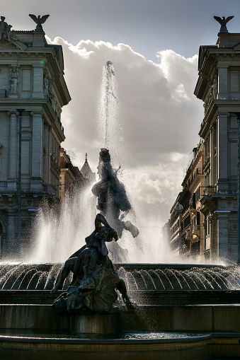 The silhouette of the beautiful Fountain of the Naiads in Piazza della Repubblica, in the heart of Rome, on the edge of the Rione Monti. The Fountain of the Naiads was built in 1870 during the pontificate of Pope Pius IX, a few days before the conquest of Rome by the troops of the Kingdom of Italy and the end of the temporal power of the papacy. In the center there is a view of the central Via Nazionale. The Monti district is a popular and multi-ethnic quarter much loved by the younger generations and tourists for the presence of trendy pubs, fashion shops and restaurants, where you can find the true soul of the Eternal City. The Rione Monti, located between Via Nazionale and the Fori Imperiali, is also rich in numerous churches in Baroque style and archaeological remains. In 1980 the historic center of Rome was declared a World Heritage Site by Unesco. Image in high definition quality.