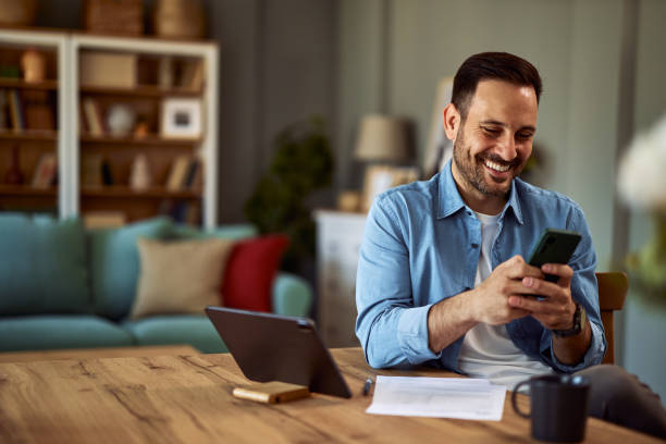 istock A cheerful man texts his friends on his phone while taking a break from his work on tablet. 1916799686