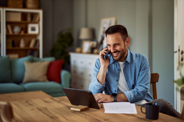 istock A smiling adult freelancer talking on a phone with a client while looking at a tablet in front of him. 1916799687
