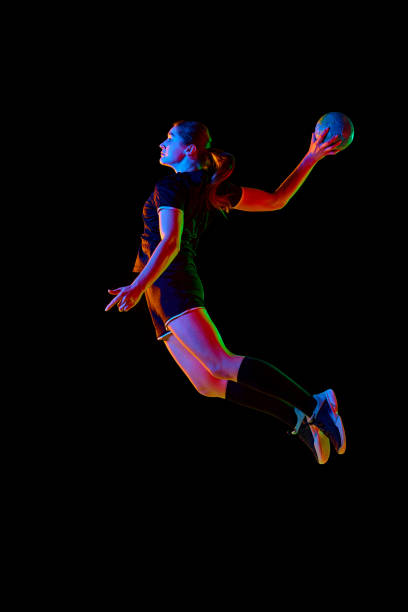istock Athletic young woman, sportsman showing handball techniques, emphasizing skill and dedication against black background in neon light. Concept of sport. 1916826457