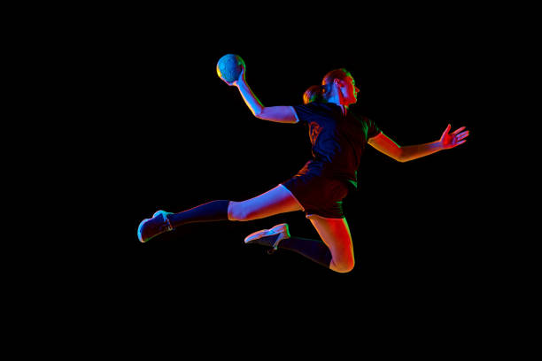 istock Determined female athlete practicing handball moves with concentration and dedication against black background in neon light. Concept of sport and action. 1916826461