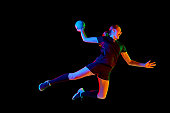 Fit, focused woman engaged in handball drills, displaying determination and focus against black background in mixed neon light. Concept of sport.