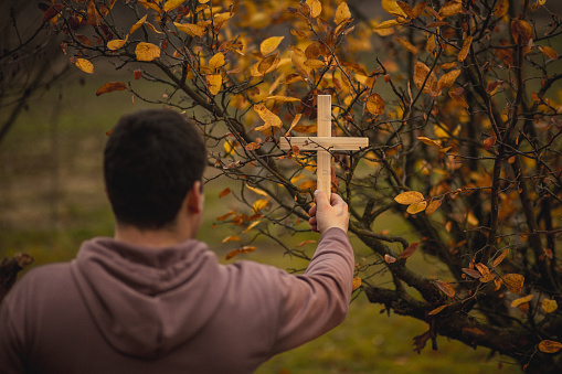 Back view of man holding religious wooden cross with nature background