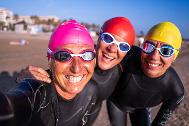 Three sportswomen friends who are open water swimmers take a selfie on a beach. stock photo