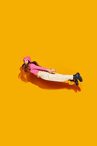 High-flying style. Fashion-forward young girl jumps in modern, comfortable clothing against vibrant yellow background. Concept of fashion and beauty, modern style, movement, shopping, sales.