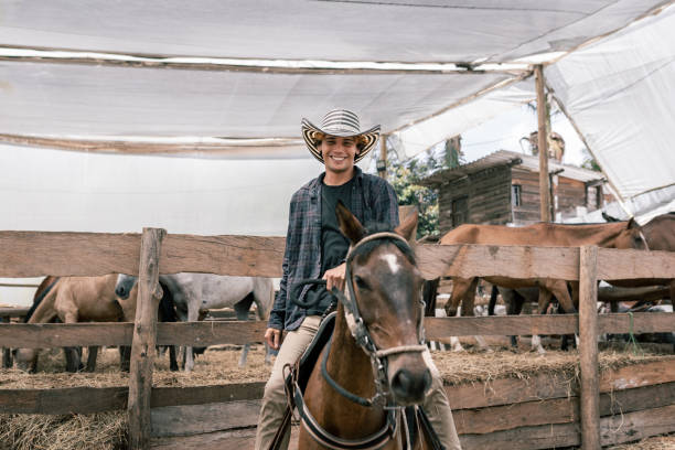 A smiling young Hawaiian man, wearing a hat, enjoys horseback riding