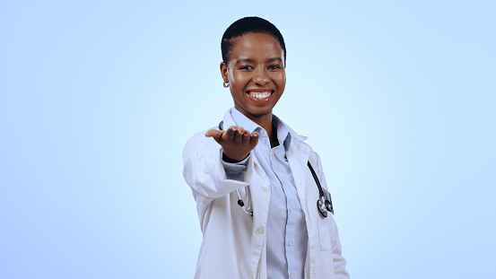 Portrait, black woman and doctor with open palm, promotion and healthcare on a blue studio background. Face, African person and professional with donation, charity and medical with welcome or support