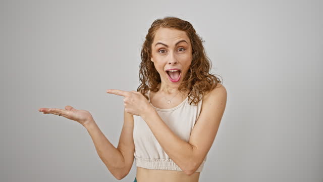 Joyful young woman standing amazed, confidently presenting and pointing with a smile, isolated on a white background