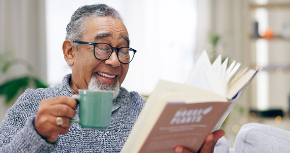 Senior man, book and coffee on sofa with smile, reading or relax in retirement in home living room. Elderly person, literature and happy with tea cup for knowledge, thinking and drink on lounge couch