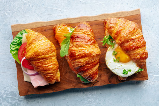 Croissant sandwich variety. Various stuffed croissants, overhead flat lay shot on a wooden board. Rolls filled with ham, salmon, egg, etc