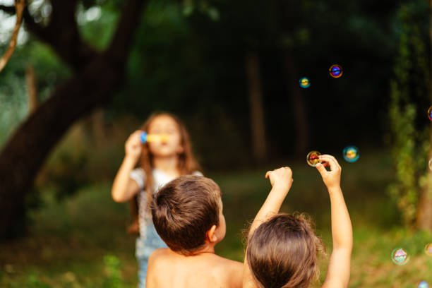 istock Child blowing soap bubbles while other friends having fun catching them in nature 1916921130