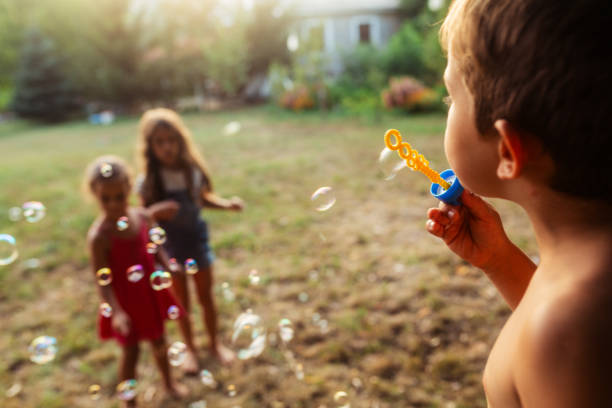 istock Child blowing soap bubbles while other friends having fun catching them in nature 1916922700