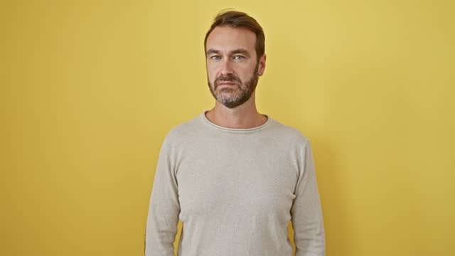 Hispanic man, standing tall, expressing a natural, simple look. serious face. staring confidently at the camera, isolated on a yellow backdrop.
