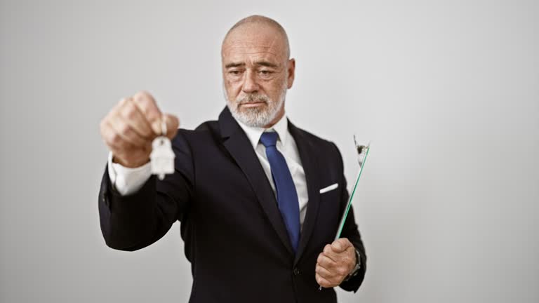 Confident, mature businessman holding keys with a white background highlighting professionalism and success.