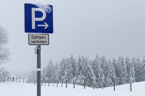 Parking lot traffic sign, but camping is prohibited. Snow-covered winter landscape with wooden pasture fence.