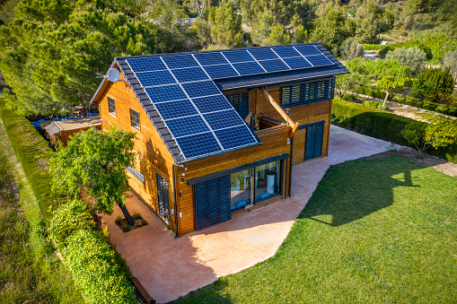 Aerial view of a Solar photovoltaic panels on a wood house roof surrounded by green vegetation
