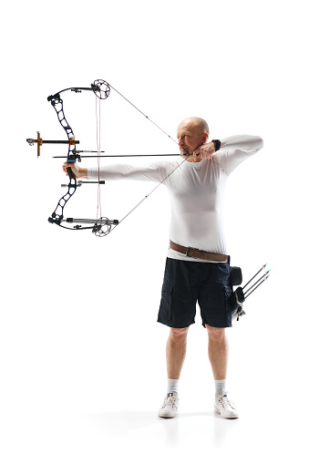 Full-length of serious man, archery sportsman aiming archery bow on target isolated over white studio background. Concept of professional sport and hobby, competition, action, game