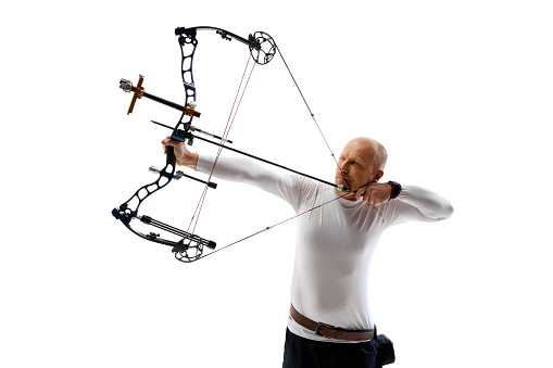 Man in his 40s, archery athlete with bow and arrow aiming at archery target isolated over white studio background. Concept of professional sport and hobby, competition, action, game