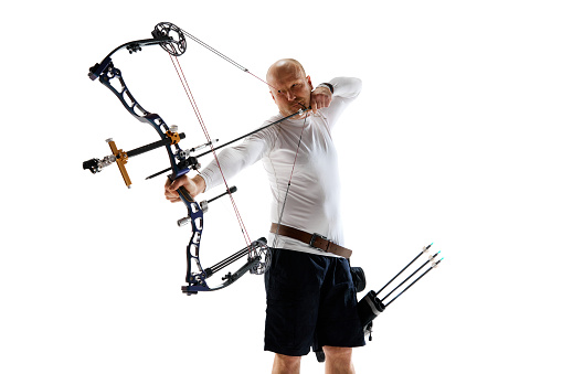 Concentrated serious man aiming with archery bow on target, training isolated over white studio background. Concept of professional sport and hobby, competition, action, game