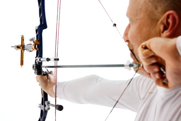 Close-up of man, archery athlete aiming with artery bow on target isolated over white studio background. Concept of professional sport and hobby, competition, action, game