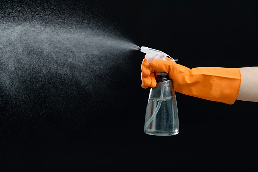 Hand using spray bottle on black background.