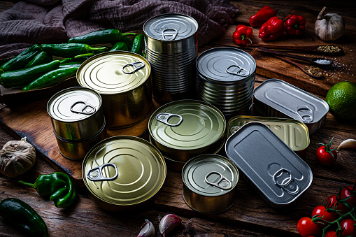 High angle view of metal tins of food of different sizes, colors and shapes shot on dark wooden table. High resolution 42Mp studio digital capture taken with Sony A7rII and Zeiss Batis 40mm F2.0 CF lens