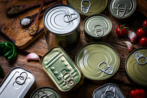 High angle view of metal tins of food of different sizes, colors and shapes shot on dark wooden table. High resolution 42Mp studio digital capture taken with Sony A7rII and Sony FE 90mm f2.8 macro G OSS lens