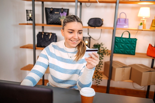 Young person begins new business with selling purses on line sitting in front of laptop